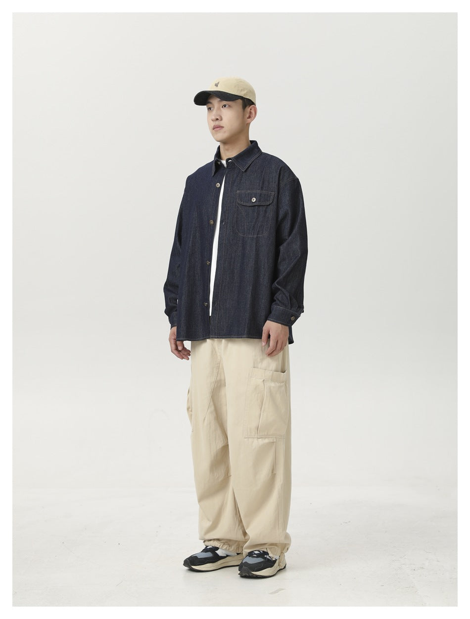 Model wearing a dark indigo denim button-front shirt, cream cargo pants, and a beige cap.