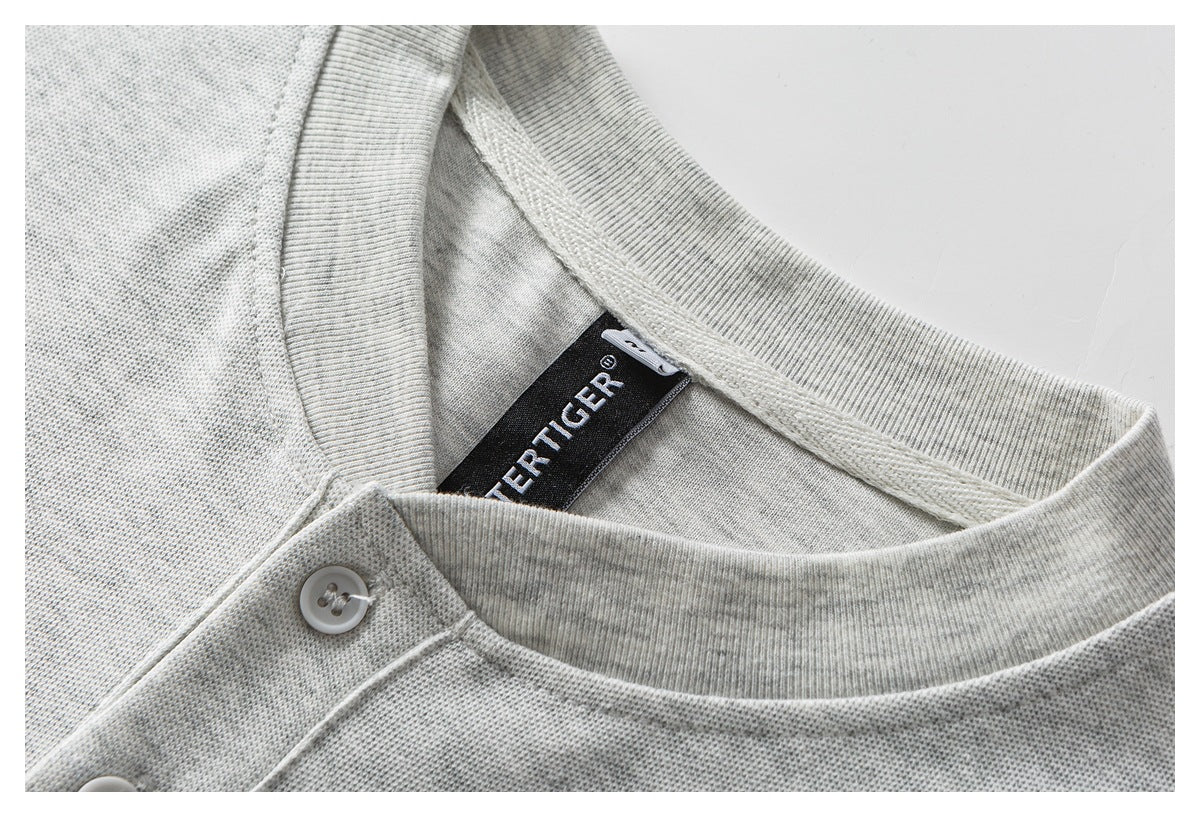 Close-up of a light gray knit shirt collar with white buttons and a black woven neck label.