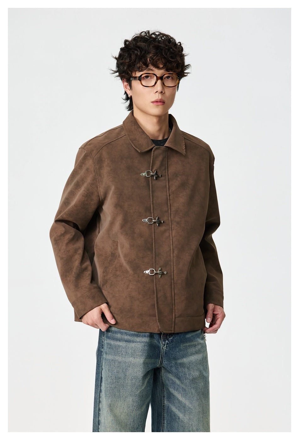 Person wearing a brown suede-look jacket with three silver metal hook closures and blue jeans, front view