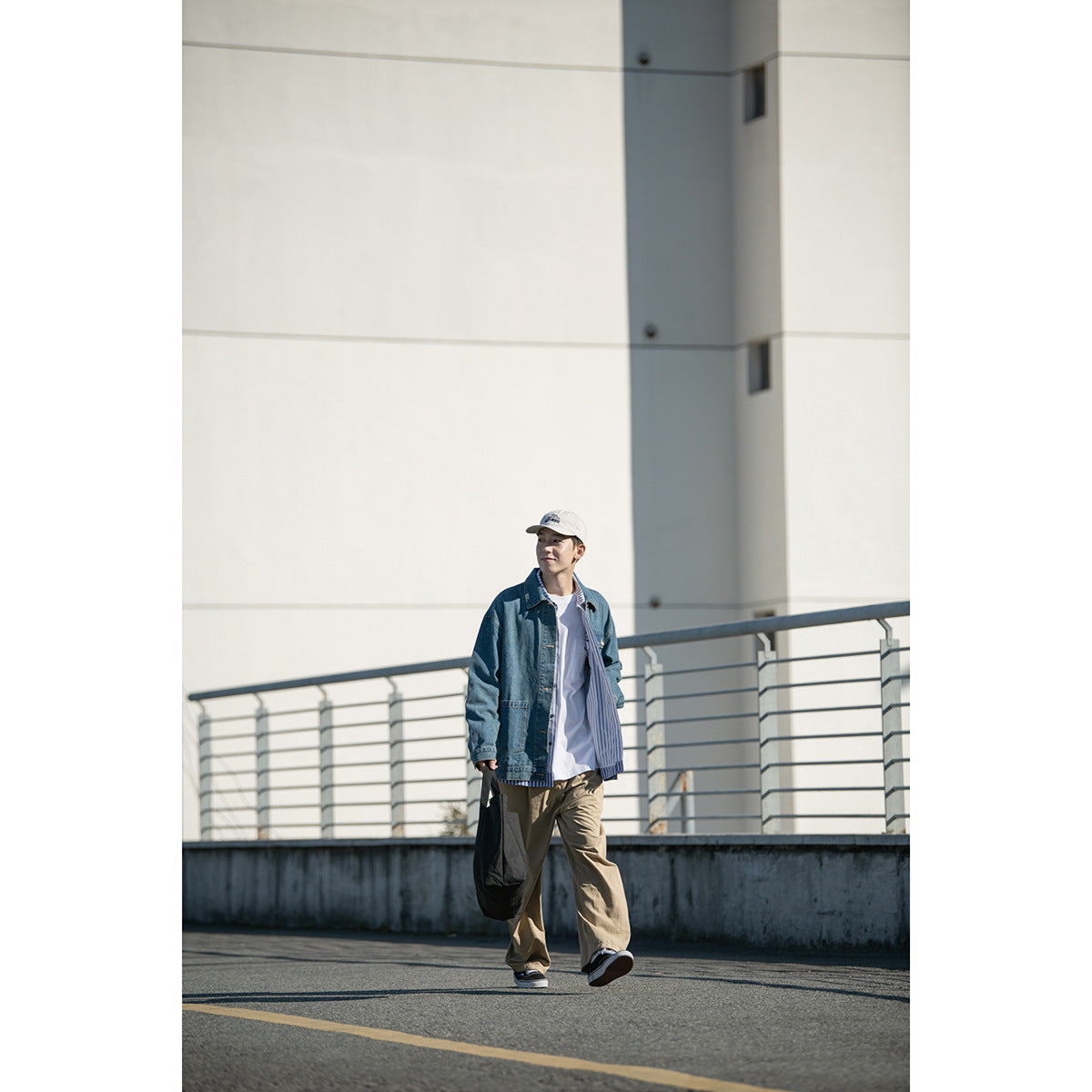 Full-length model wearing a blue denim jacket, striped shirt, and loose tan trousers outdoors.