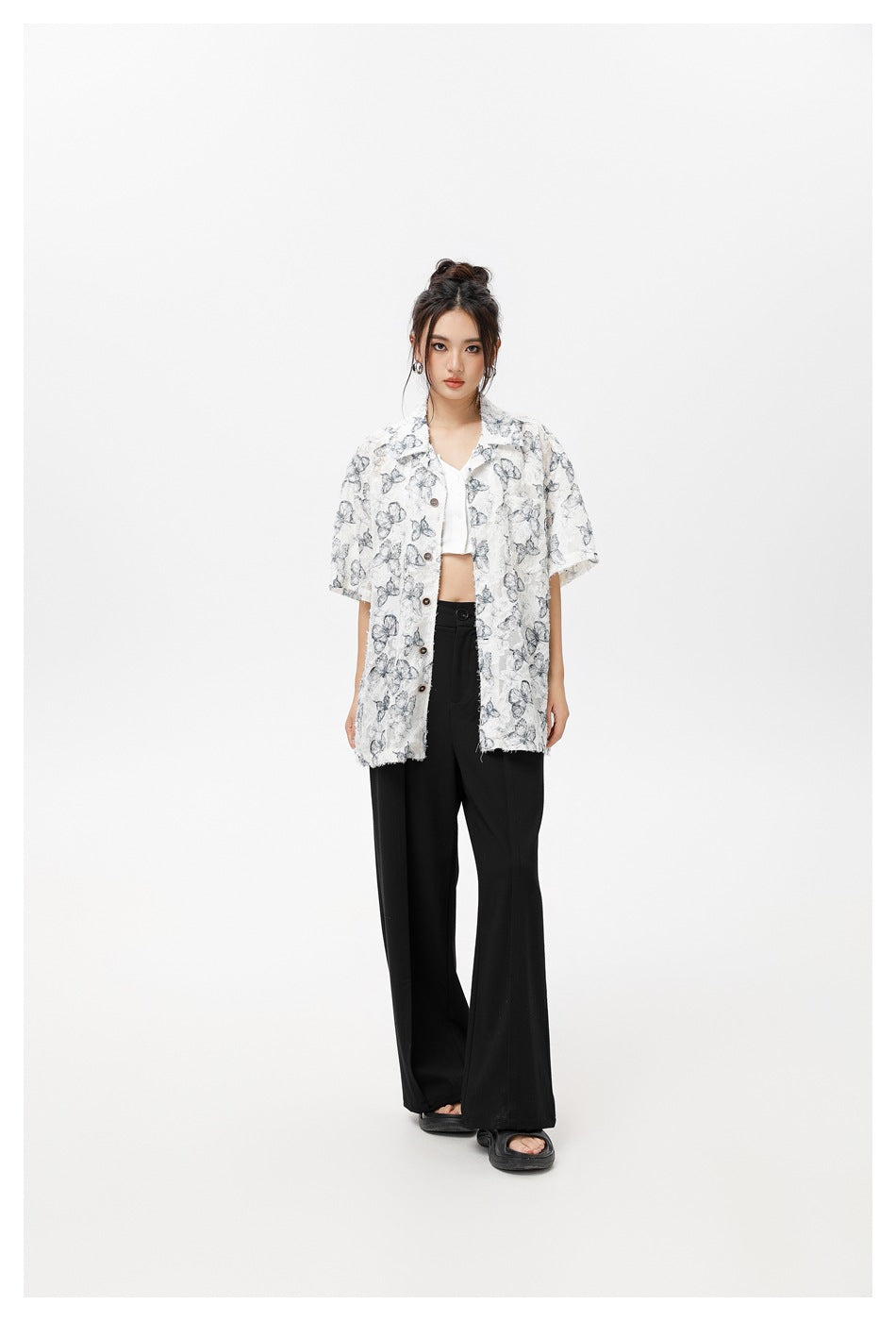 Model wearing an oversized white short-sleeve button-up shirt with gray-blue butterfly prints and black trousers.