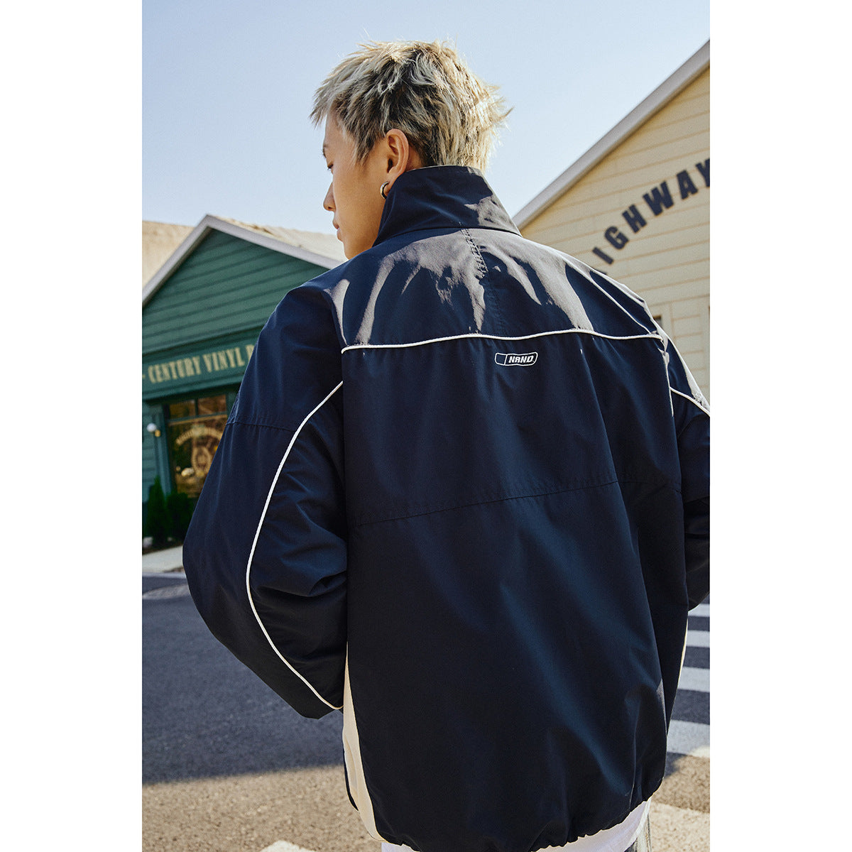 Model wearing a navy jacket with white piping, shown from the back.