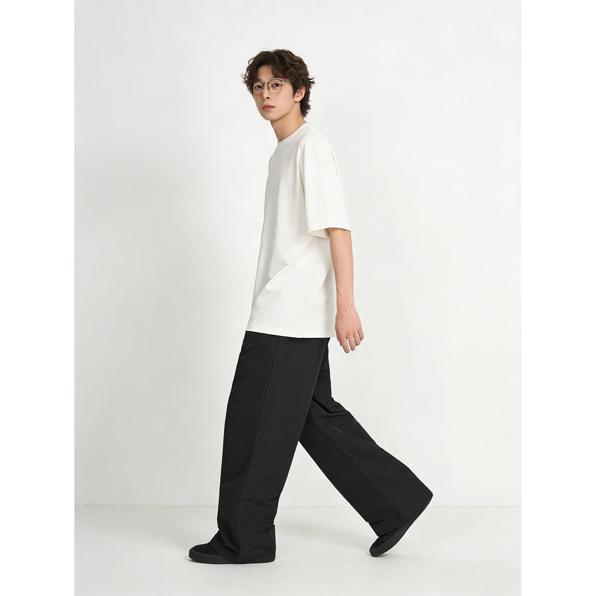 Side view of a model wearing a white oversized T-shirt with loose black trousers while walking.