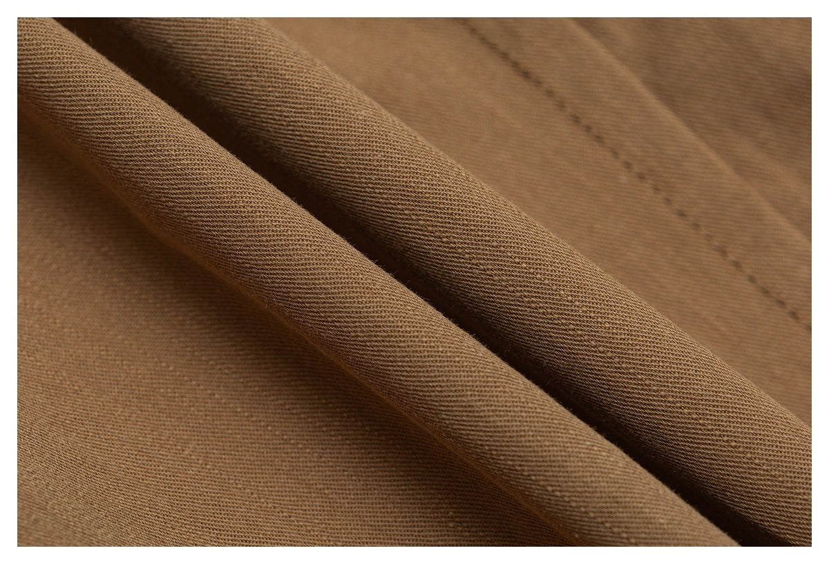 Extreme close-up of the brown-tan trouser fabric showing its woven texture and stitching.