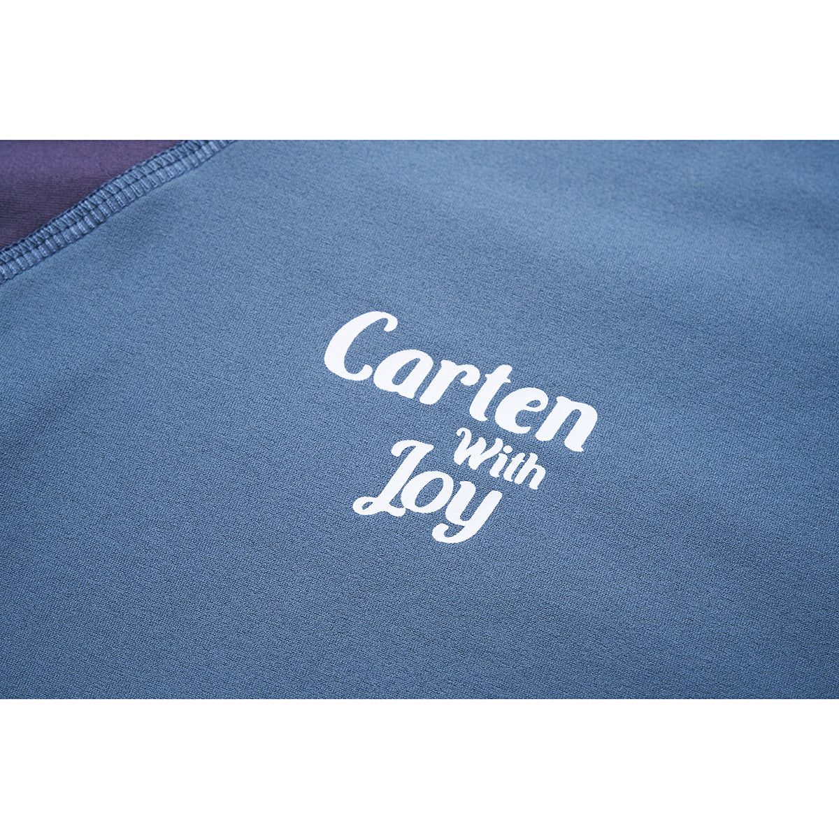 Close-up of blue fabric with white “Carten With Joy” lettering and a visible overlocked seam.