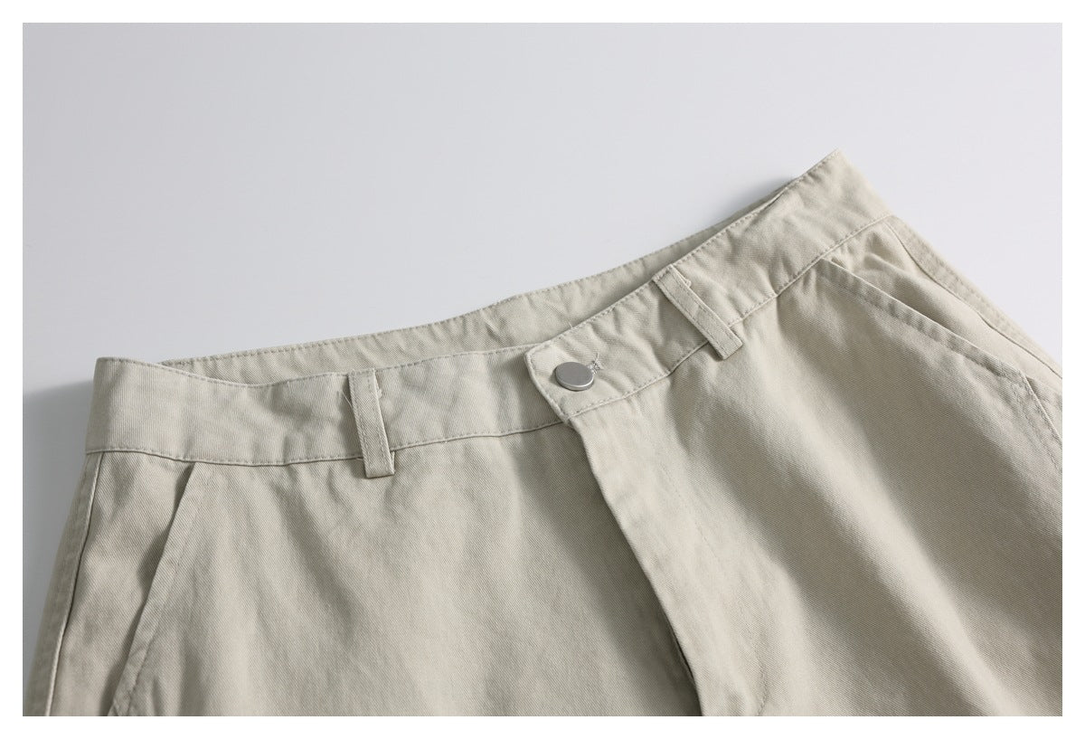 Close-up of light beige shorts showing the waistband, belt loops, metal button and front fly.