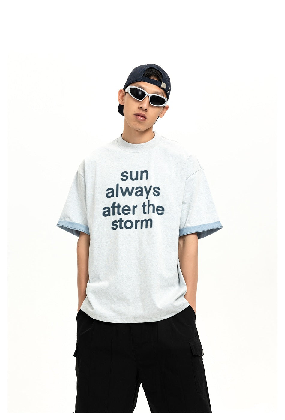 Closer front view of a model in a light gray T-shirt reading “sun always after the storm,” with blue sleeve cuffs.