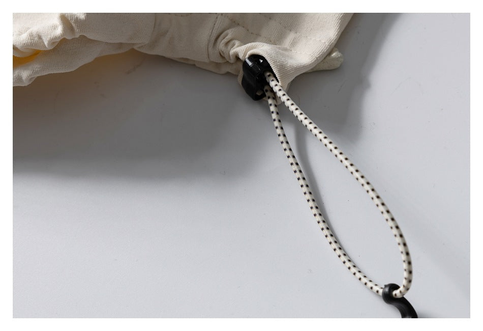 Close-up of an ivory garment hem with a black cord lock and black-dotted drawcord.