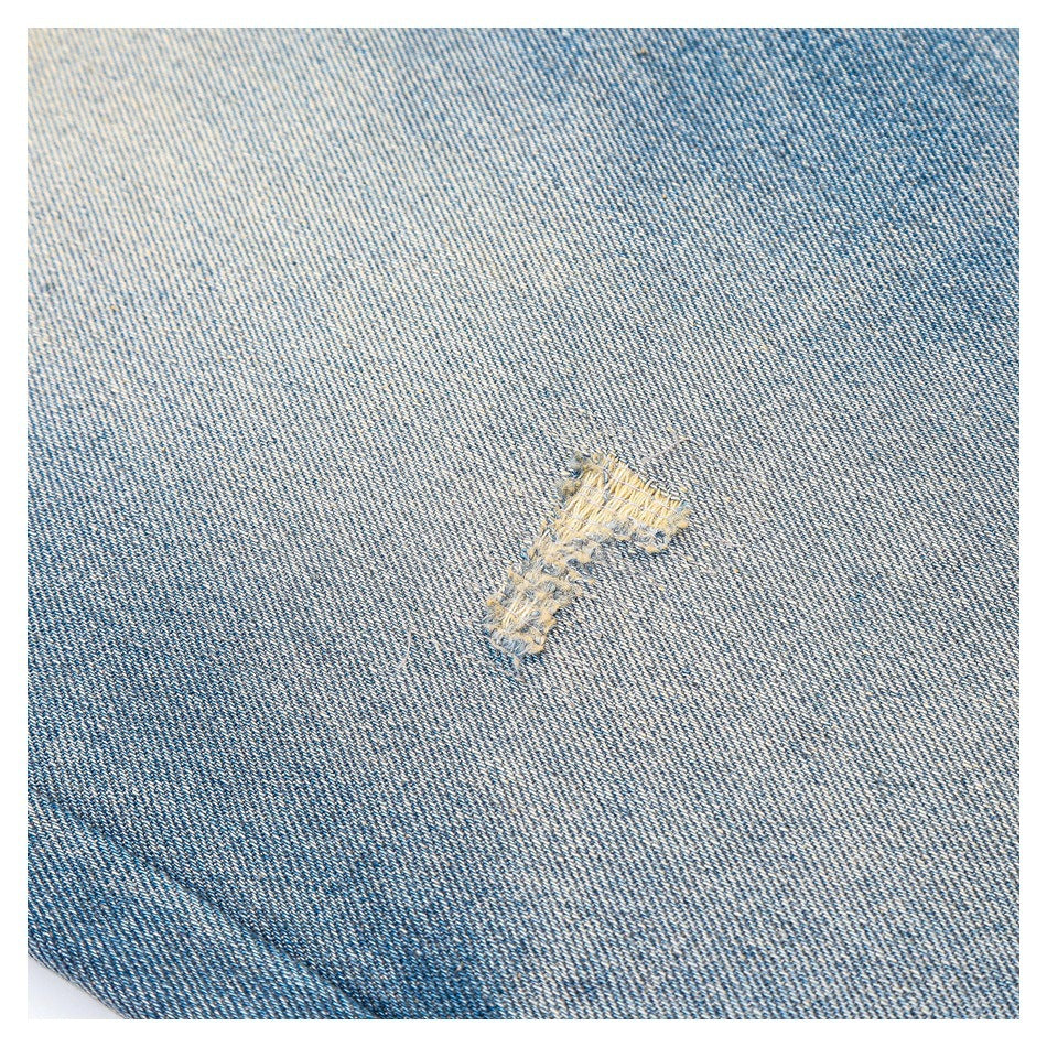 Close-up of a small distressed patch on faded blue denim.
