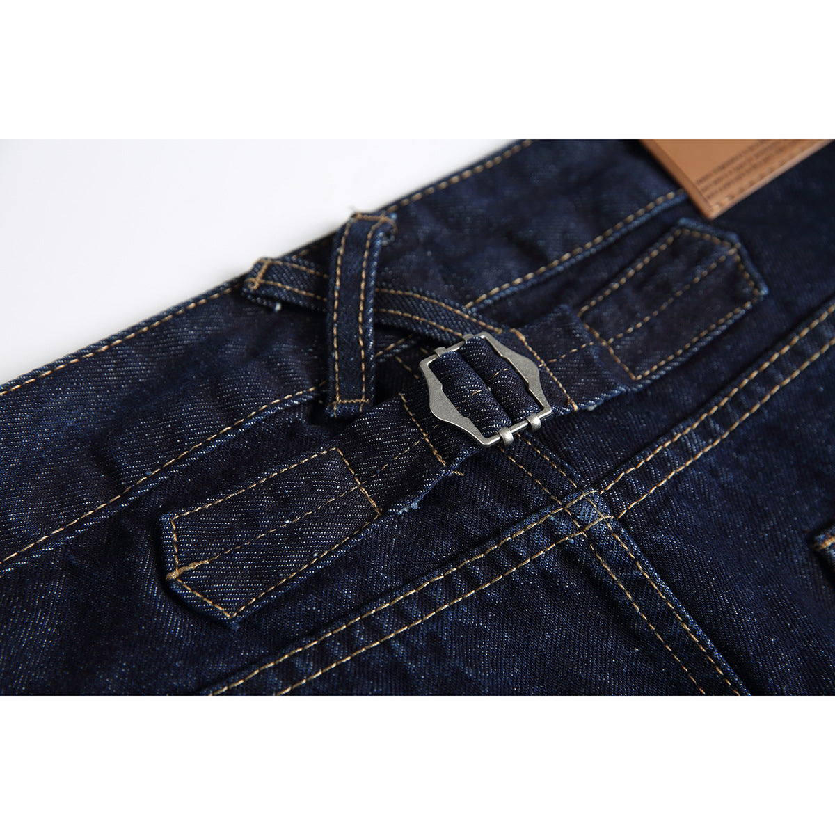 Close-up of dark indigo denim waistband with a silver buckle, belt loops and tan contrast stitching.
