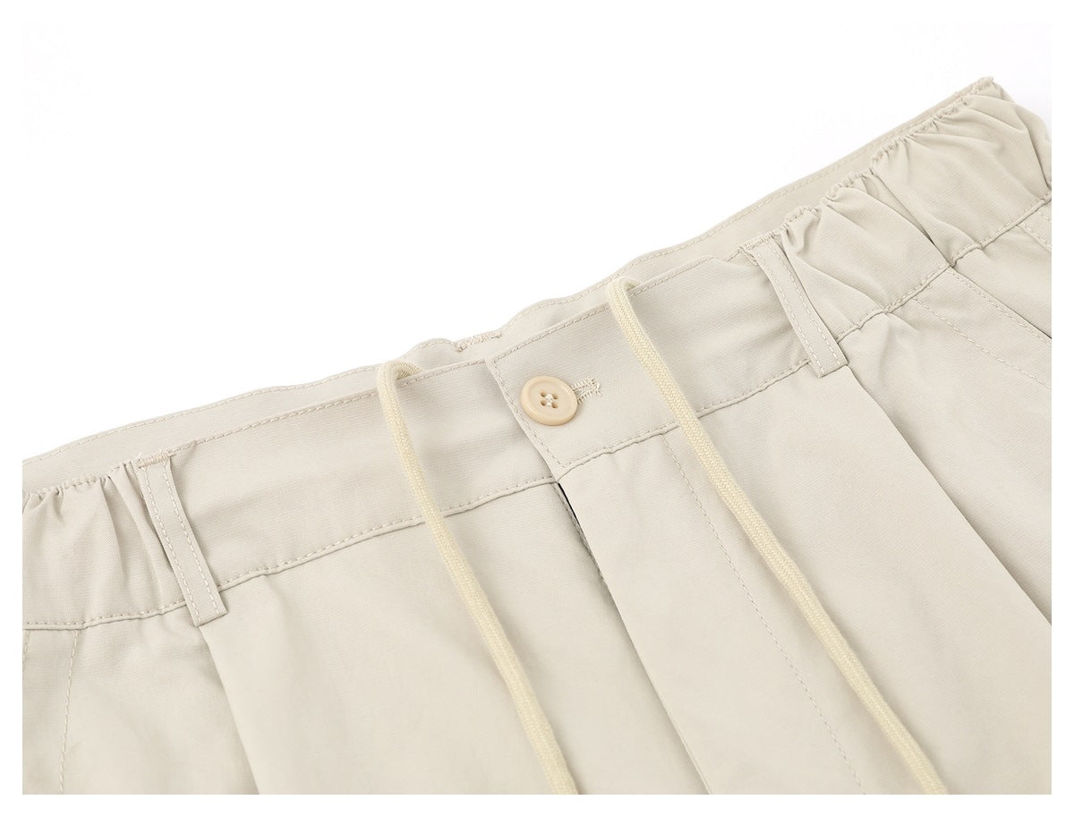 Close-up of the light beige trousers' gathered waistband, button, belt loops and drawstrings.