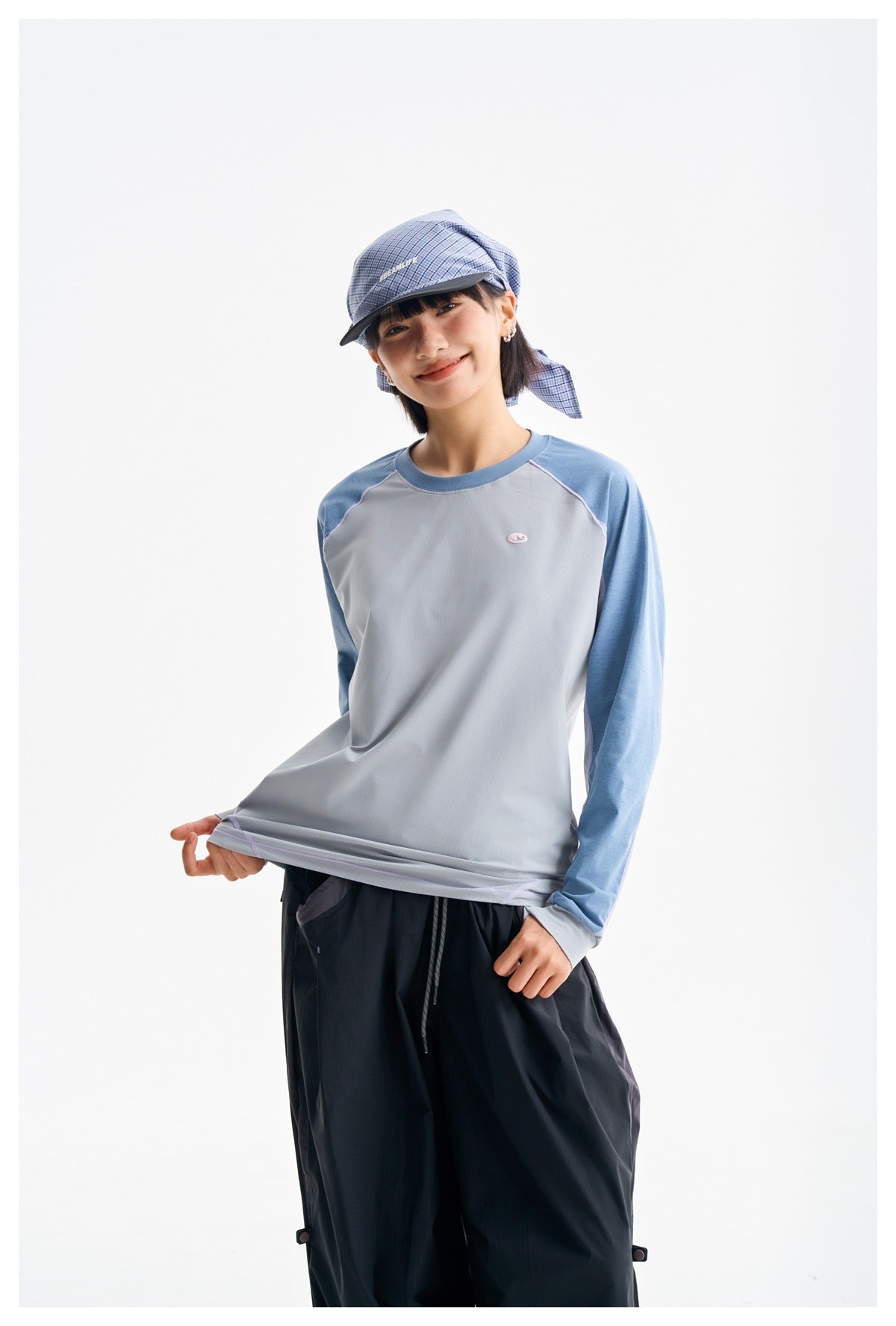 Model wears a light gray long-sleeve top with blue sleeves and loose dark pants, shown from the waist up.