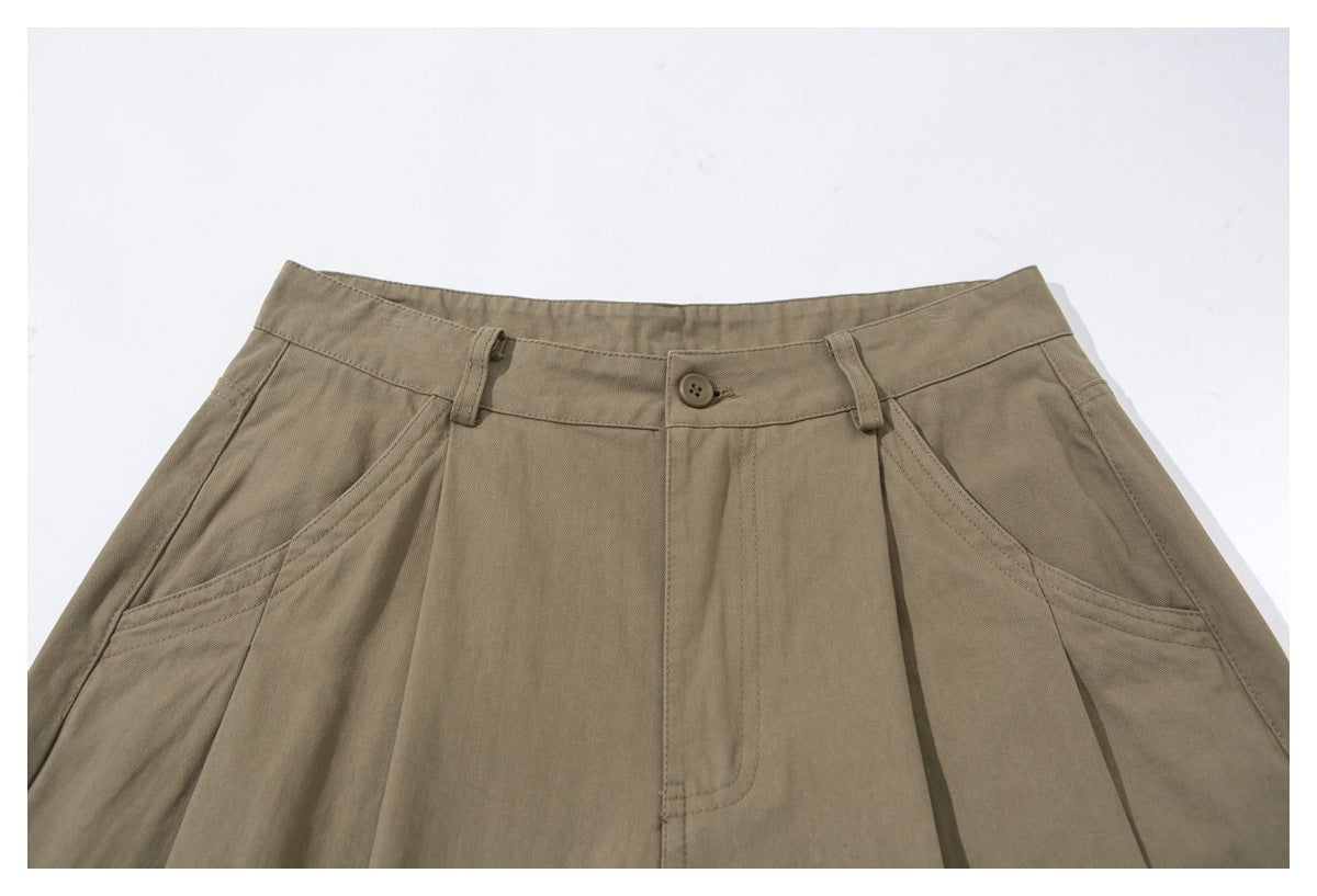 Close-up of taupe trousers showing the buttoned waistband, belt loops, pleats, and slanted front pockets.