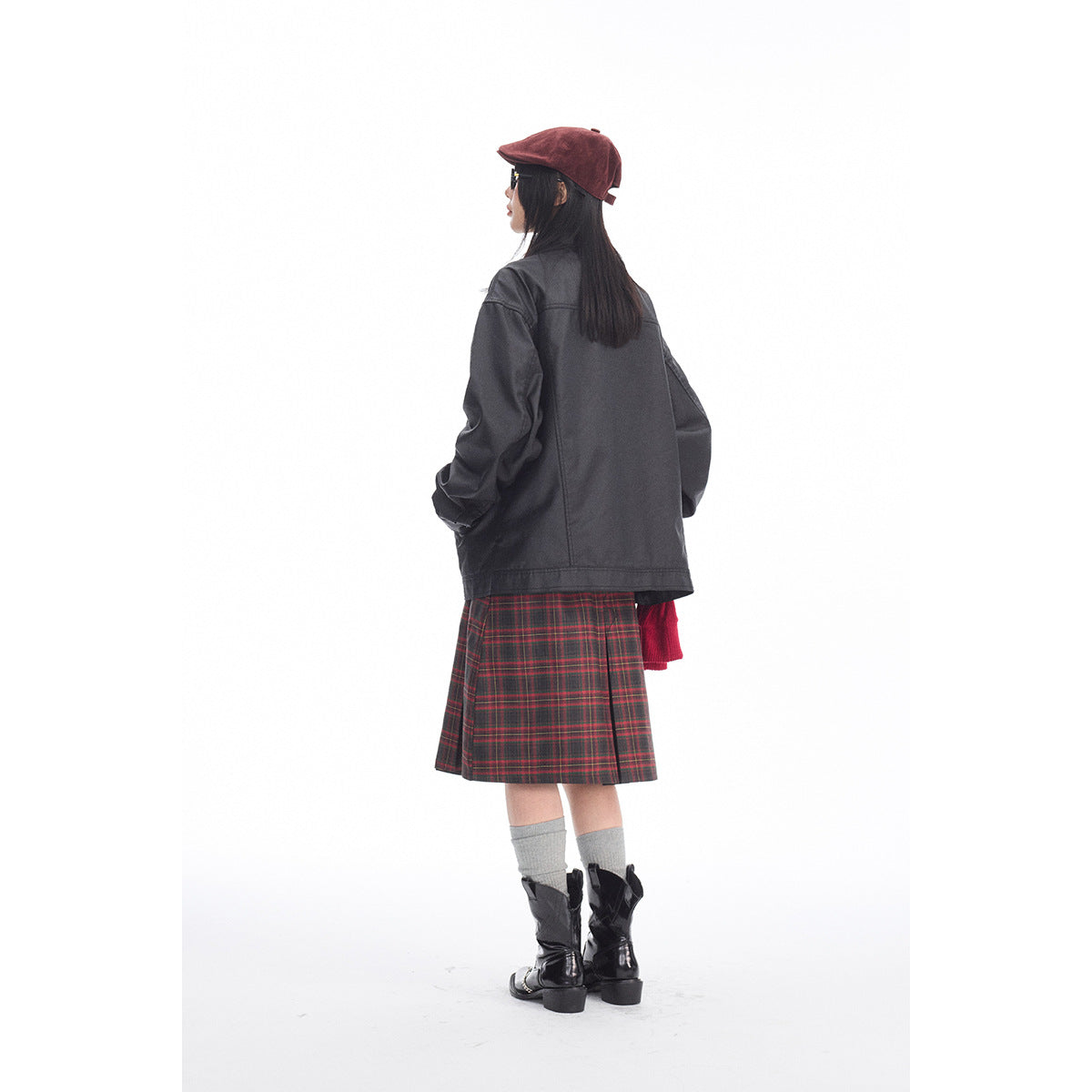 Rear view of a model in a charcoal jacket and red-and-black plaid skirt, with a burgundy cap and black boots.
