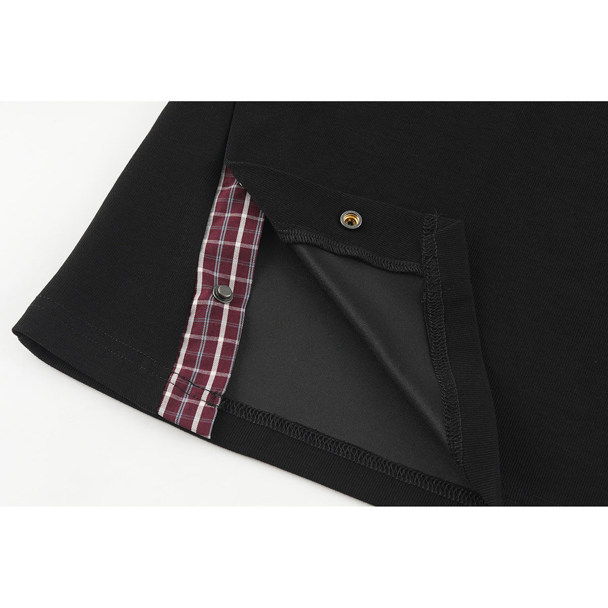 Close-up of a black shirt hem opened to show red-and-white plaid trim and snap fasteners.