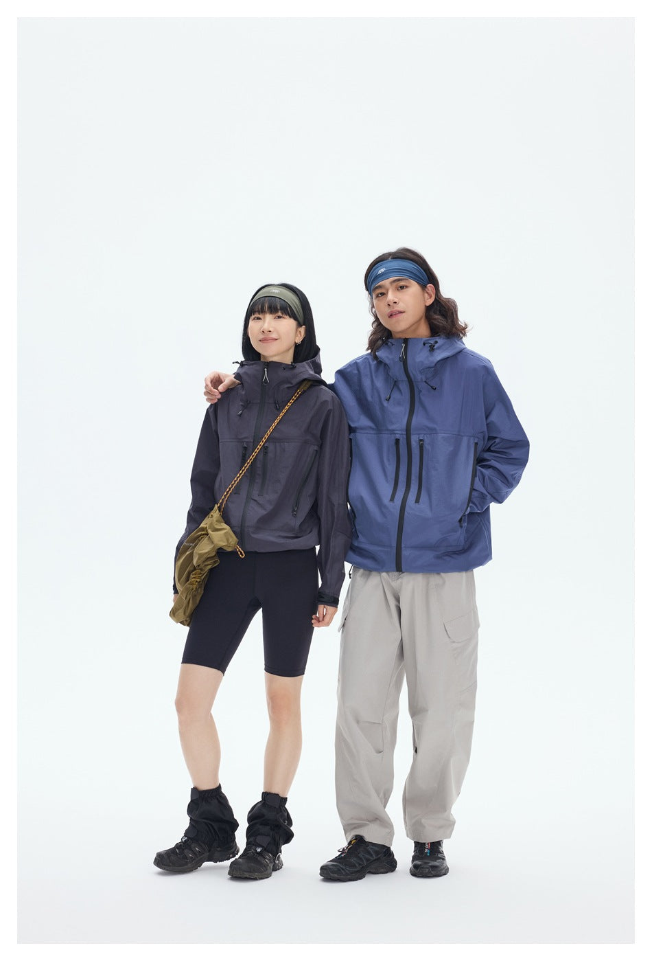 Two models wear charcoal and blue hooded outdoor jackets with front zippers and pockets; full-length studio view.