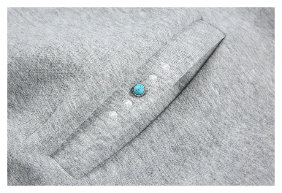 Close-up of a turquoise button and white embellishments on a light gray hoodie panel.