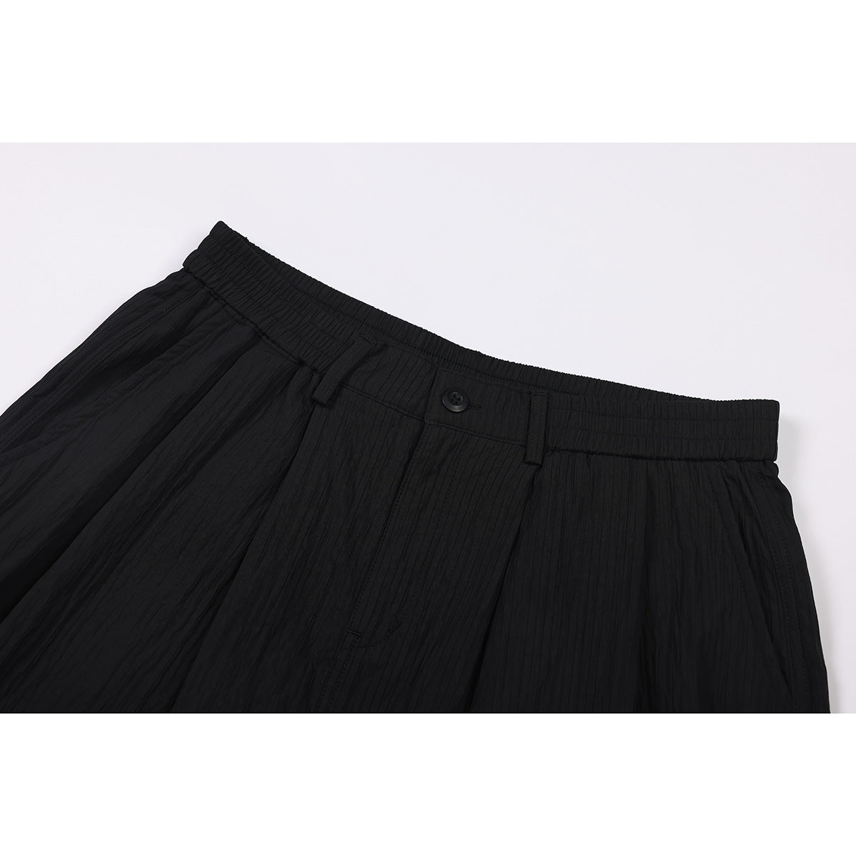 Close-up of black shorts showing the gathered waistband, belt loops, button, and textured vertical fabric.