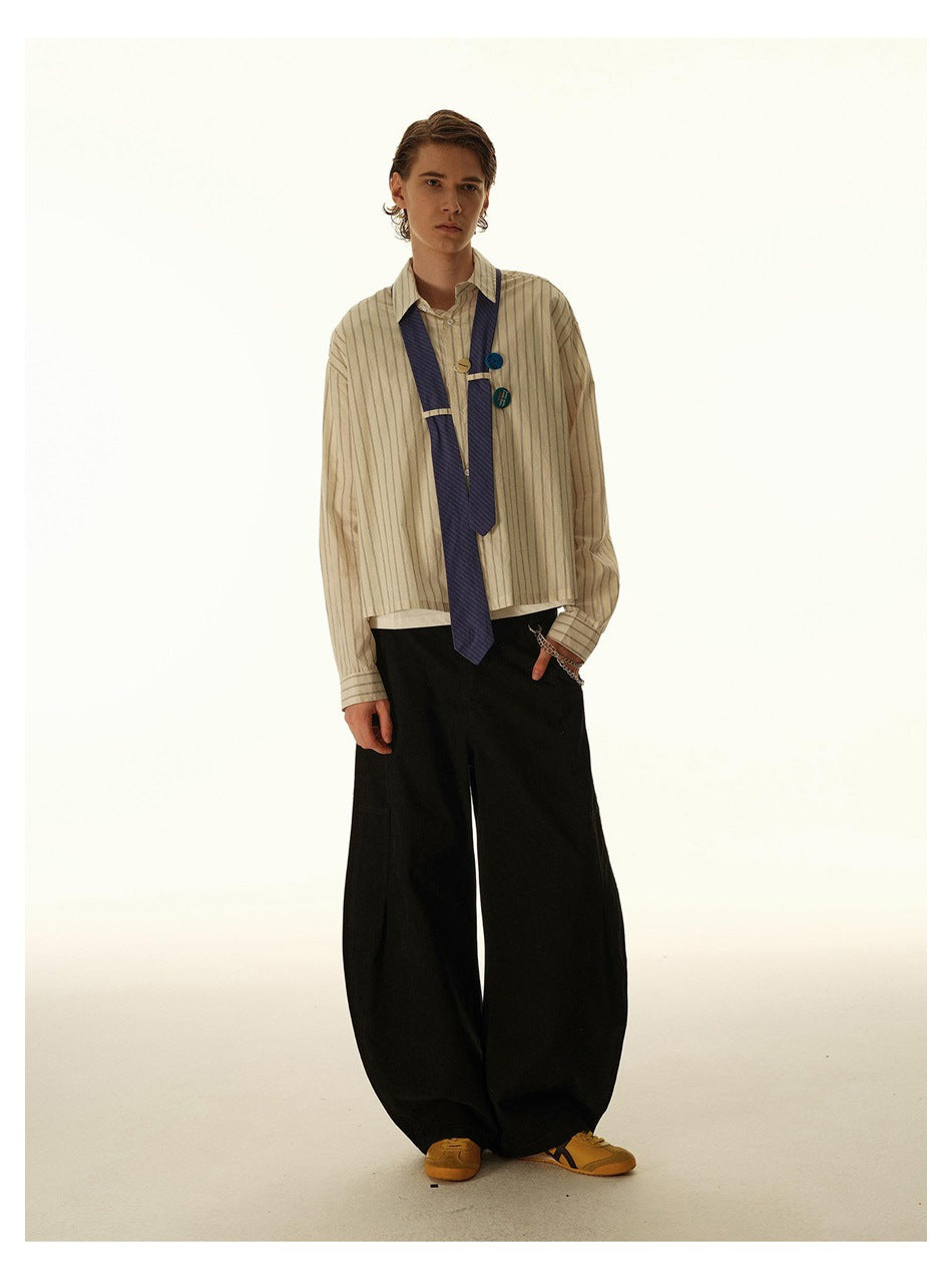 Full-length model wearing a beige striped shirt with a navy tie and pins, wide black trousers, and mustard sneakers.