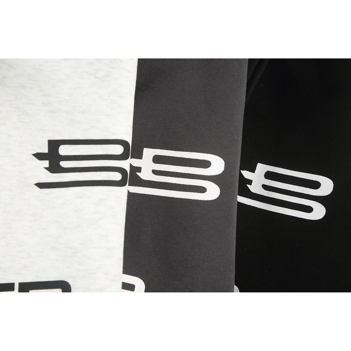 Close-up of a stylized white emblem printed on light gray, charcoal, and black garment colorways.