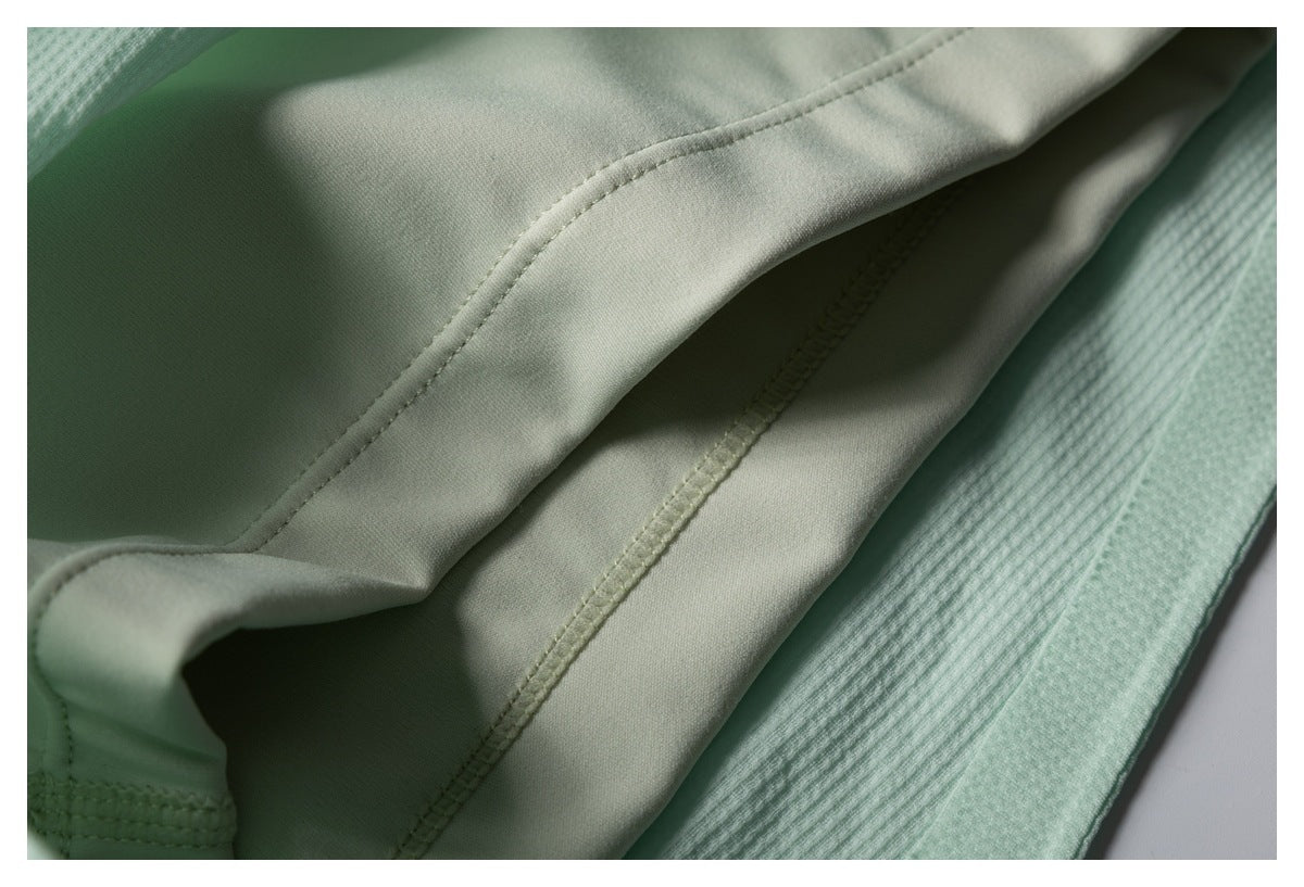 Close-up of pale mint-green fabric showing curved stitched seams beside a textured ribbed edge.