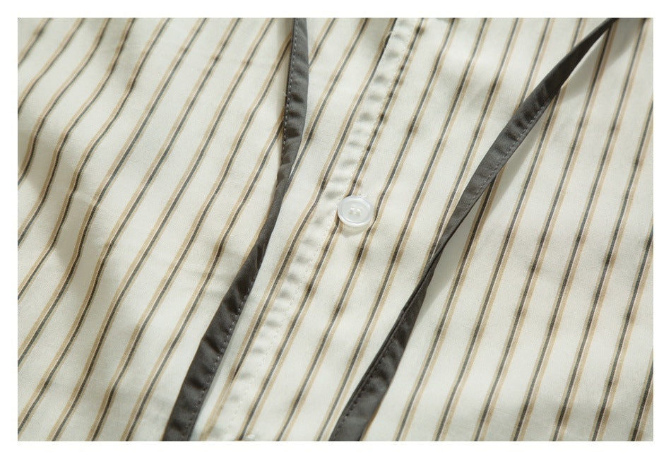 Close-up of the cream shirt's striped front, showing a white button and dark gray placket trim.