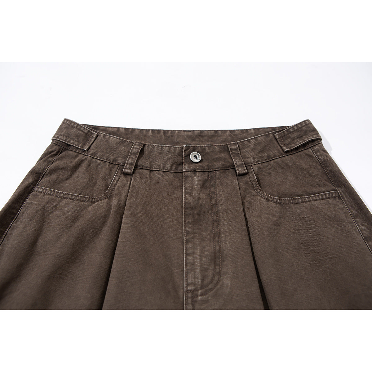 Close-up of brown trousers showing the waistband, button, belt loops, front pleats and curved pockets.