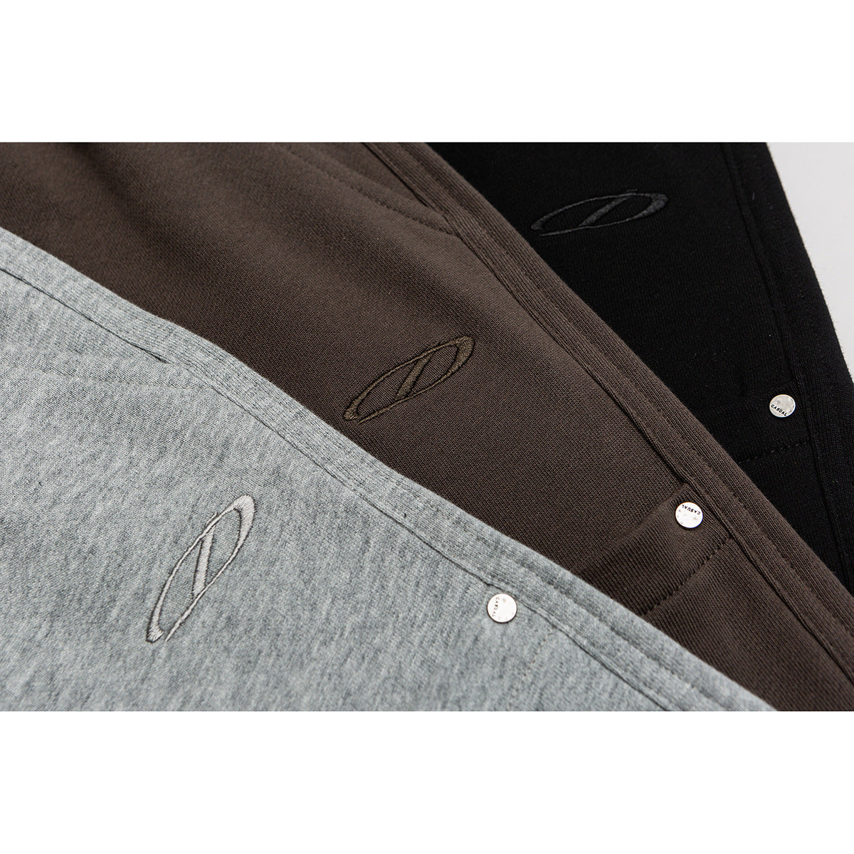 Close-up of gray, brown, and black shorts showing embroidered oval motifs and small metal snaps.