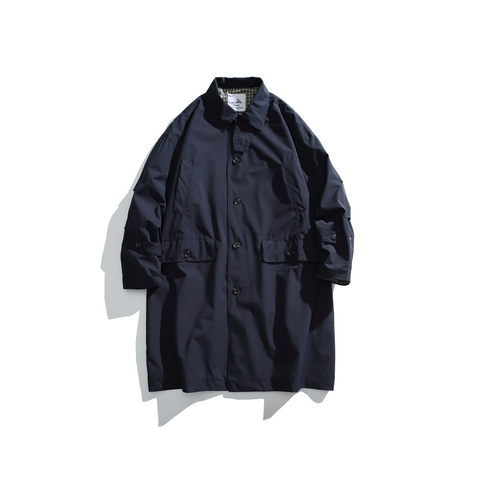 Front view of a dark navy long coat with a button closure, collar, flap pockets, and plaid lining at the cuffs.