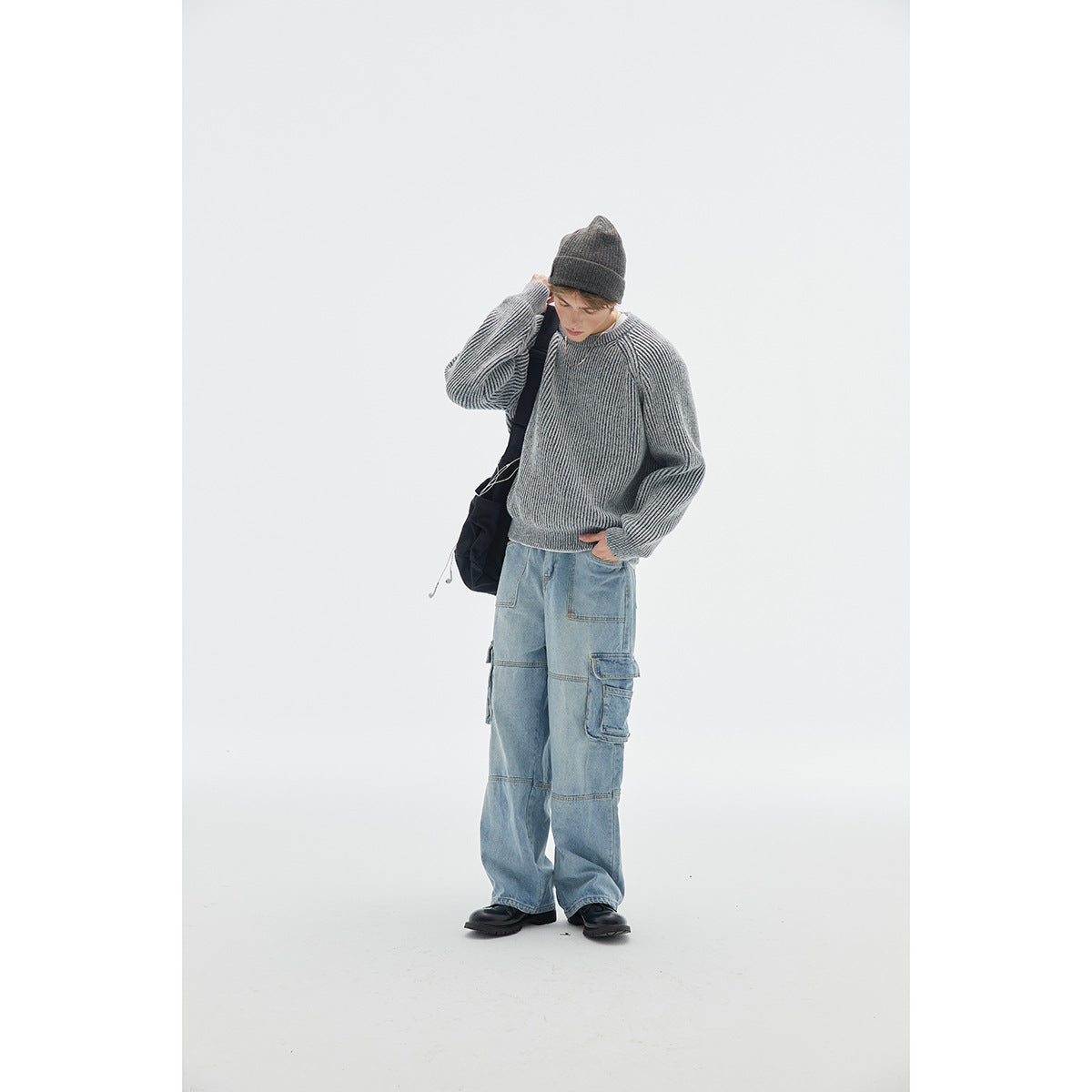 Model wearing a gray ribbed raglan sweater with a dark beanie, light blue cargo jeans, and a black shoulder bag.