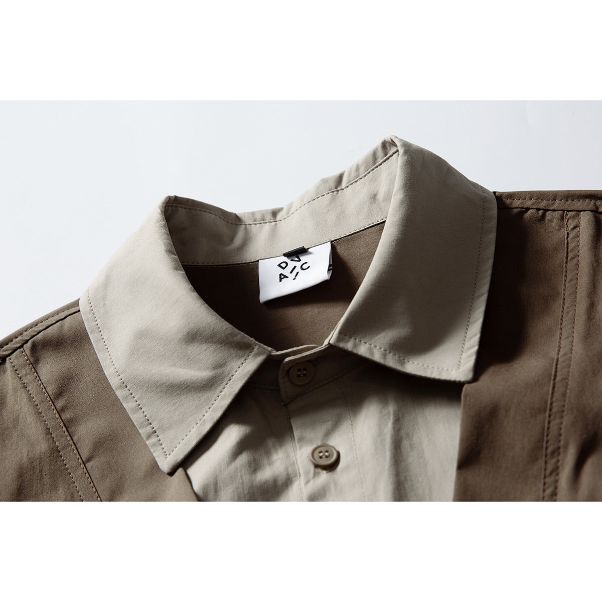 Close-up of a taupe pointed shirt collar beneath a brown vest, with buttons and a small neck label.