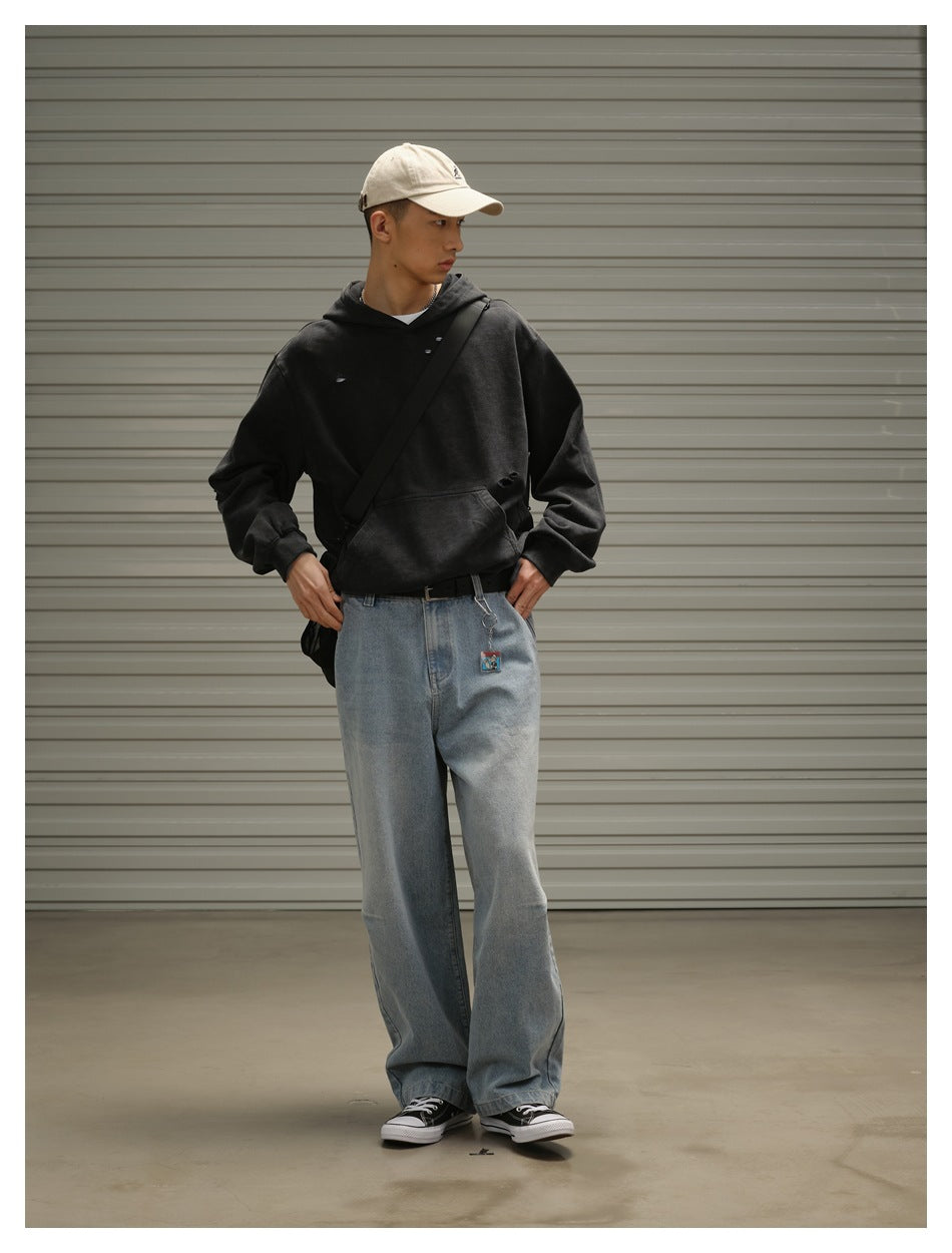 Model wearing a black distressed hoodie and pale blue wide-leg jeans, with a cream cap and black crossbody bag.