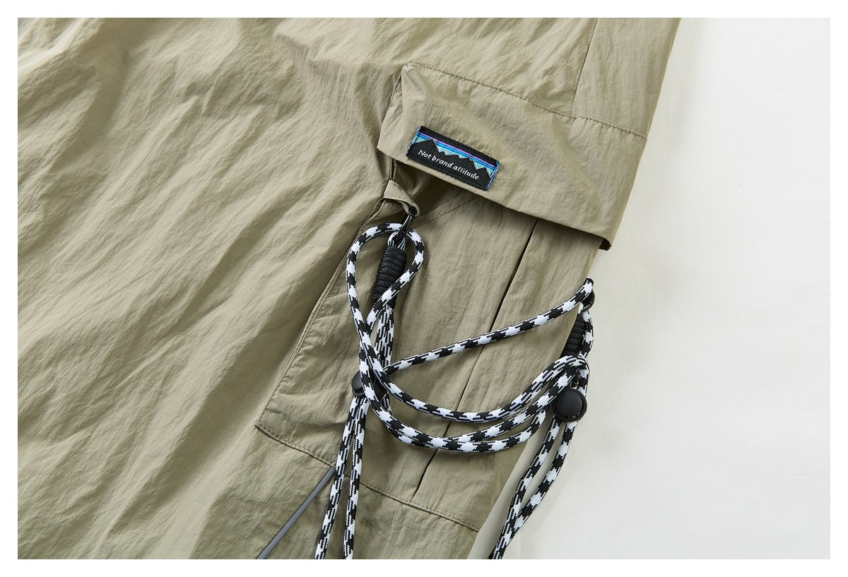 Close-up of khaki shorts with a flap pocket, black-and-white cord detail, and a small sewn label.