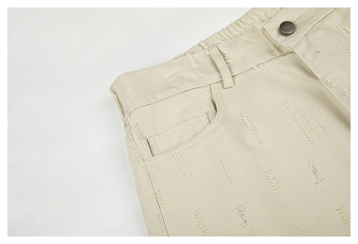 Angled close-up of cream trousers with a front pocket, belt loop, metal button and raised stitch details.
