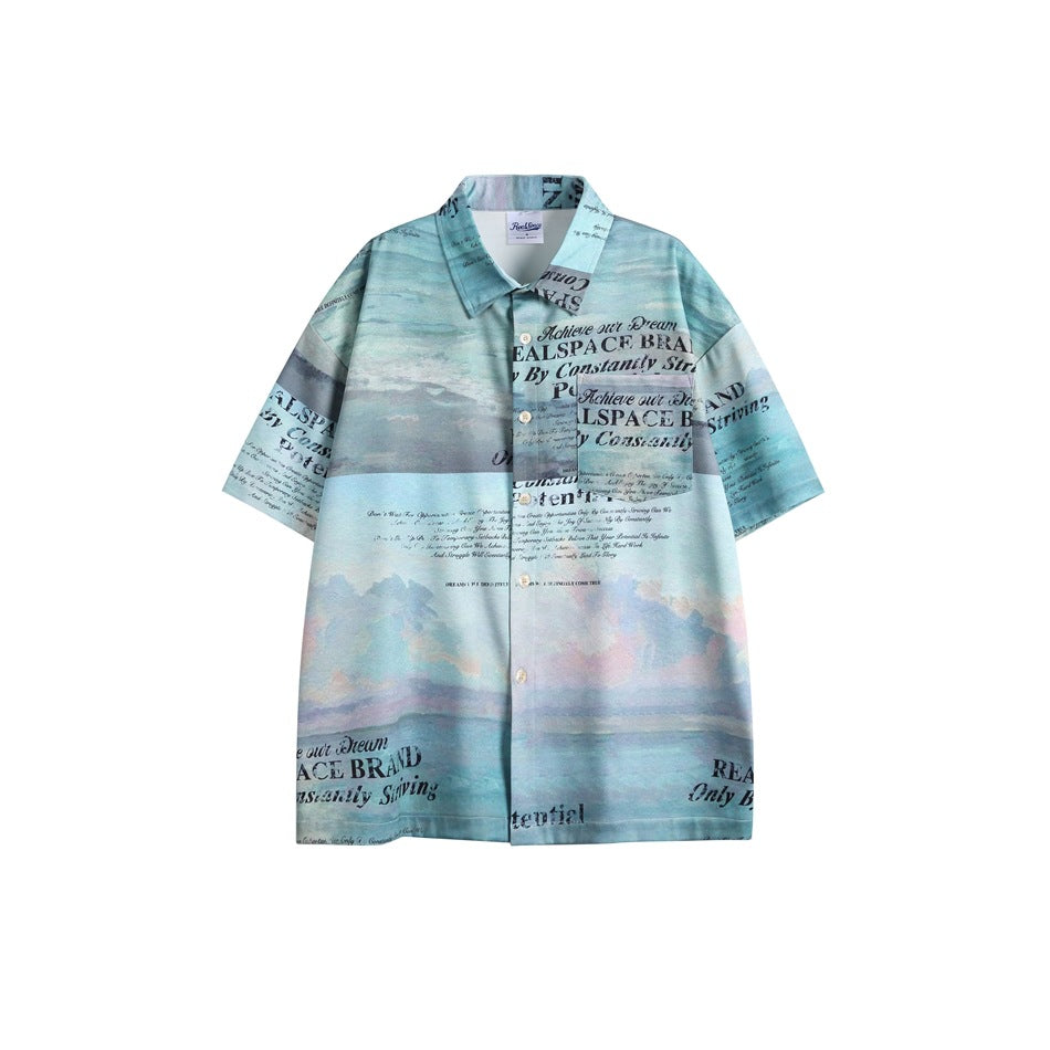 Blue-teal short-sleeve button-up shirt with painterly sky and sea print, slogan text and chest pocket, flat view