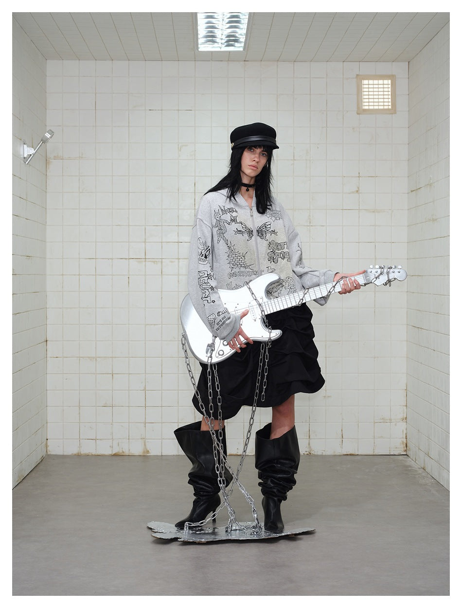 Model wearing a gray graphic zip-up hoodie, layered black skirt, and slouchy black boots while holding a guitar.
