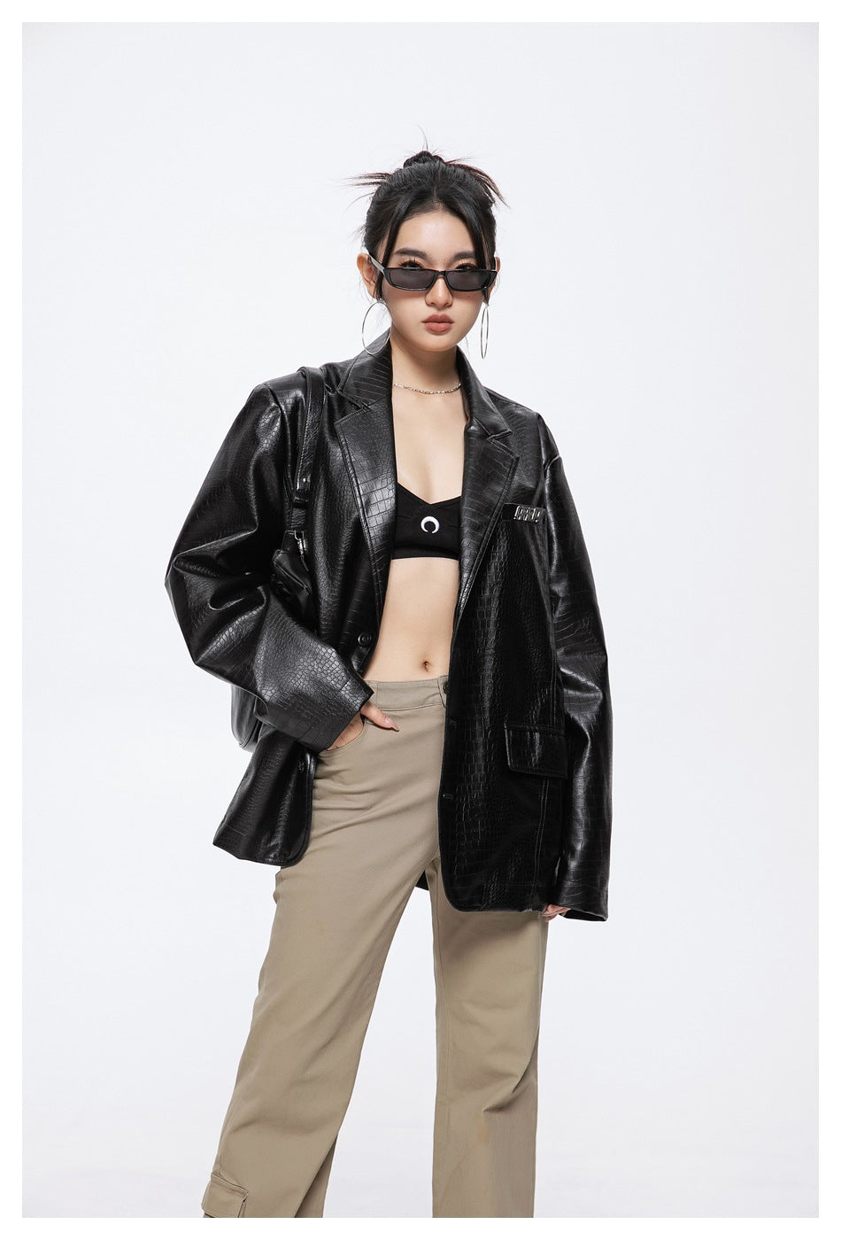 Model wearing an open black crocodile-embossed blazer over a black crop top with beige trousers.