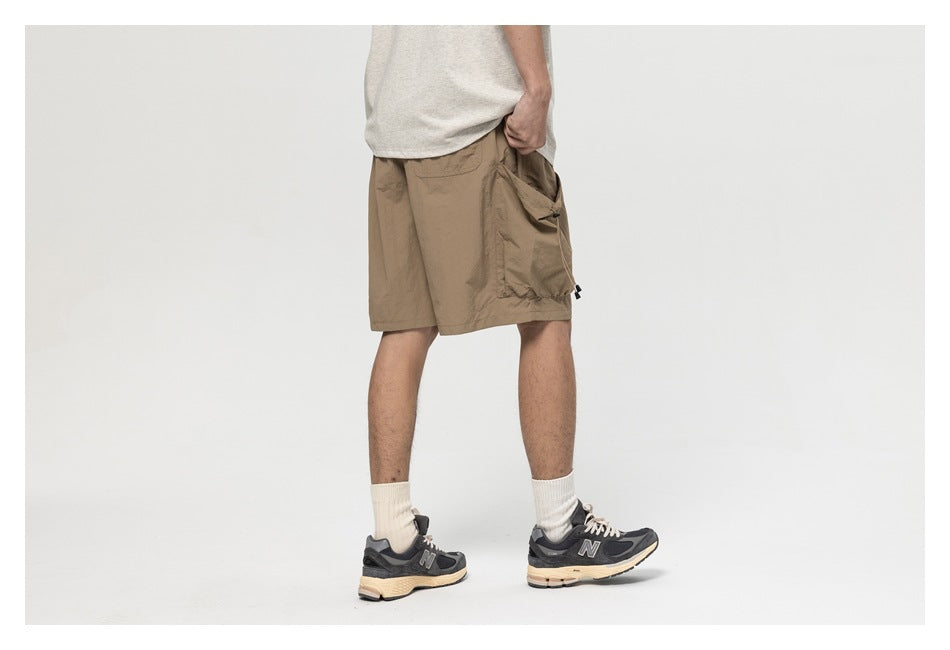 Model wearing taupe cargo shorts, shown from the back with a large drawcord side pocket.