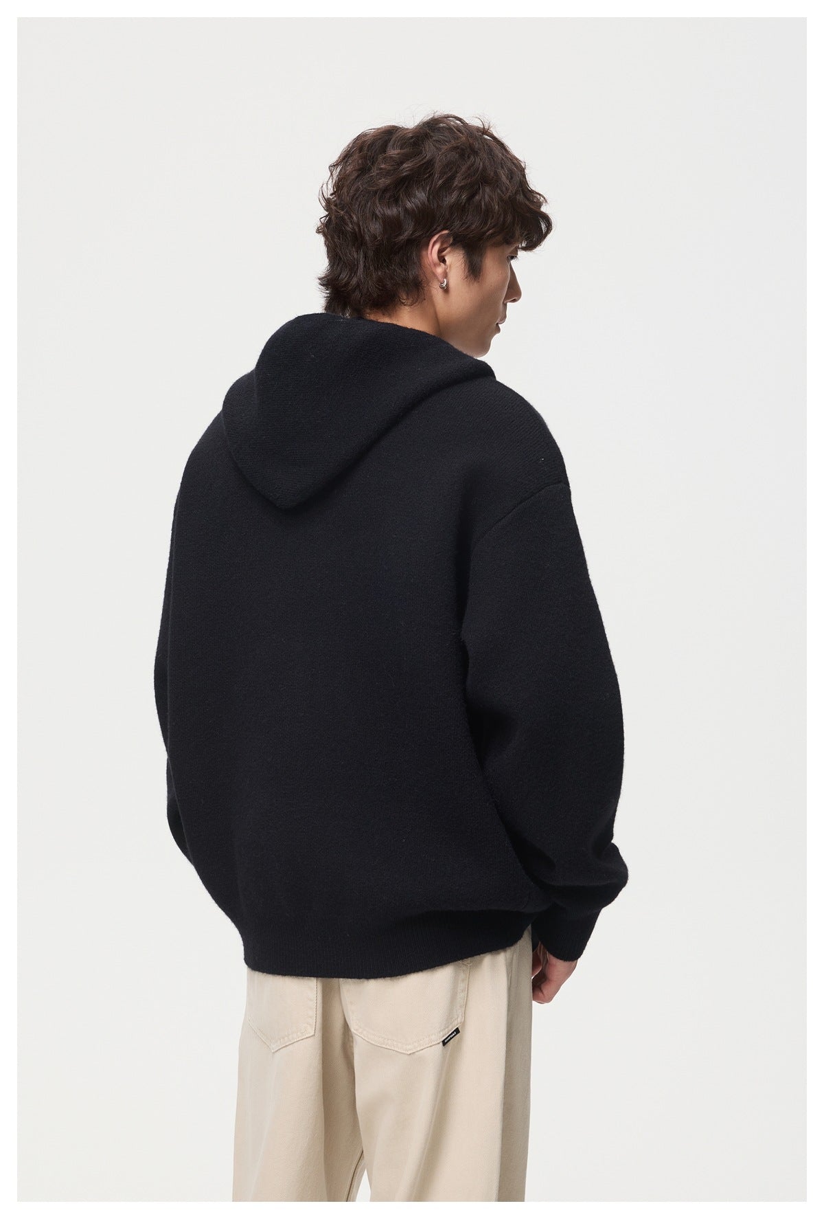 Rear view of a model wearing a black hooded cardigan with beige trousers.