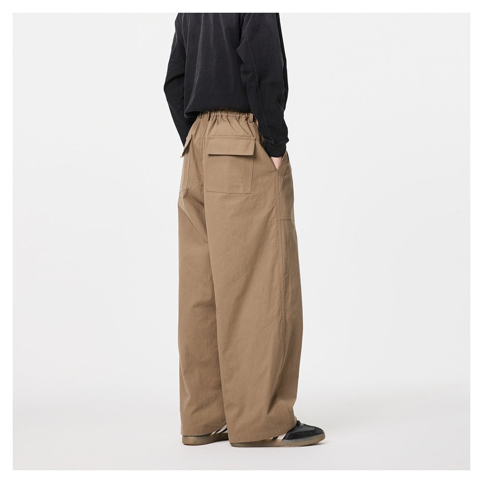 Rear view of a model wearing loose tan wide-leg trousers with flap-covered back pockets and an elasticated waist.
