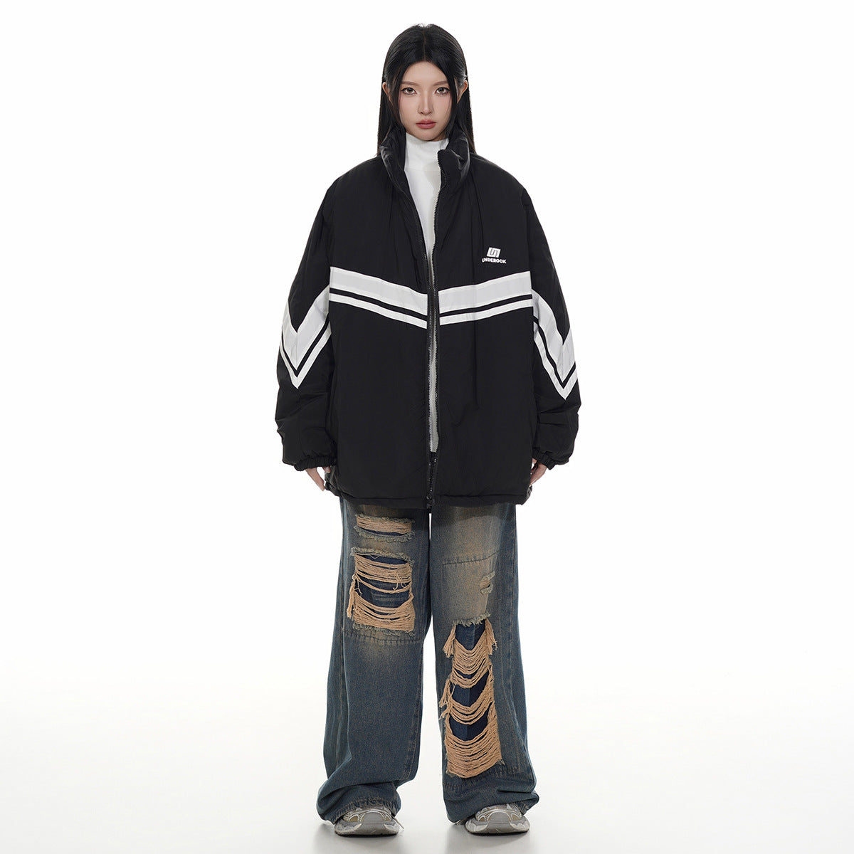 Model wearing a black oversized zip jacket with white chevron stripes and distressed wide-leg jeans, front view.