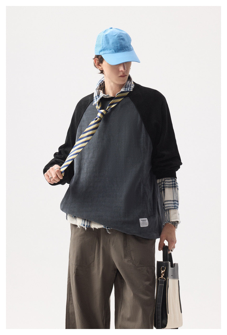 Closer front view of a model in a charcoal pullover with black raglan sleeves and a plaid shirt.