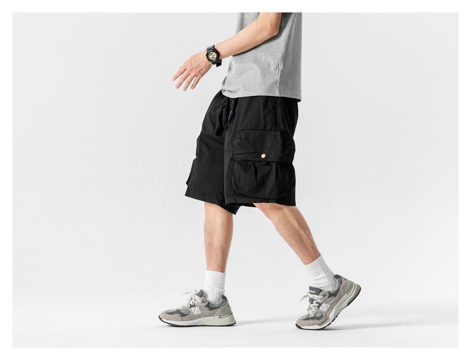 Side view of a model wearing black cargo shorts with a large buttoned flap pocket.