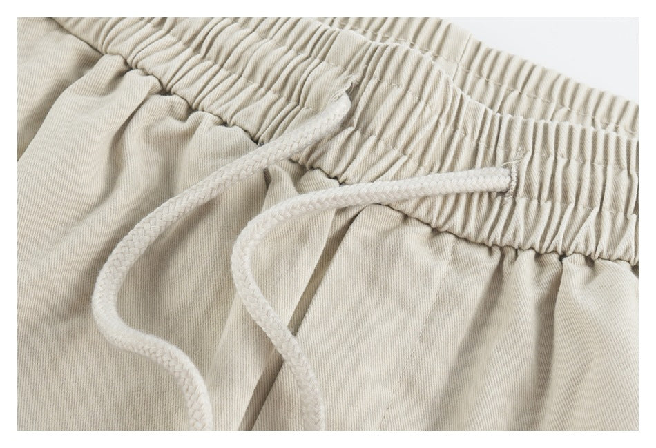 Close-up of the gathered waistband and braided drawstrings on beige shorts.