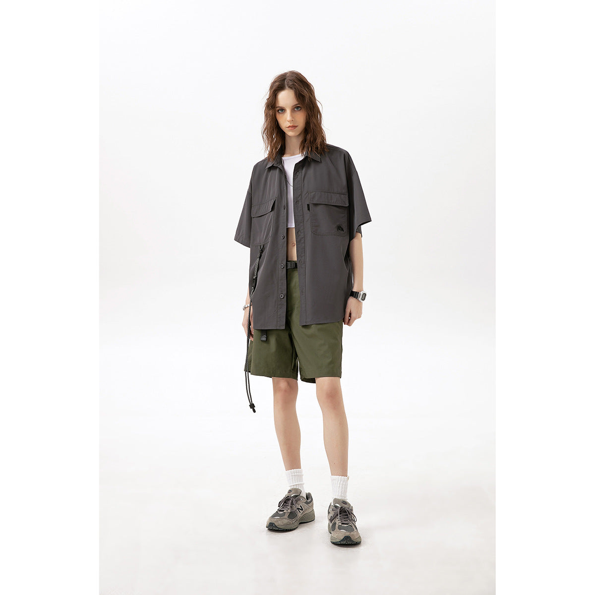 Model wearing an oversized charcoal short-sleeve button-up shirt with chest pockets and olive shorts.