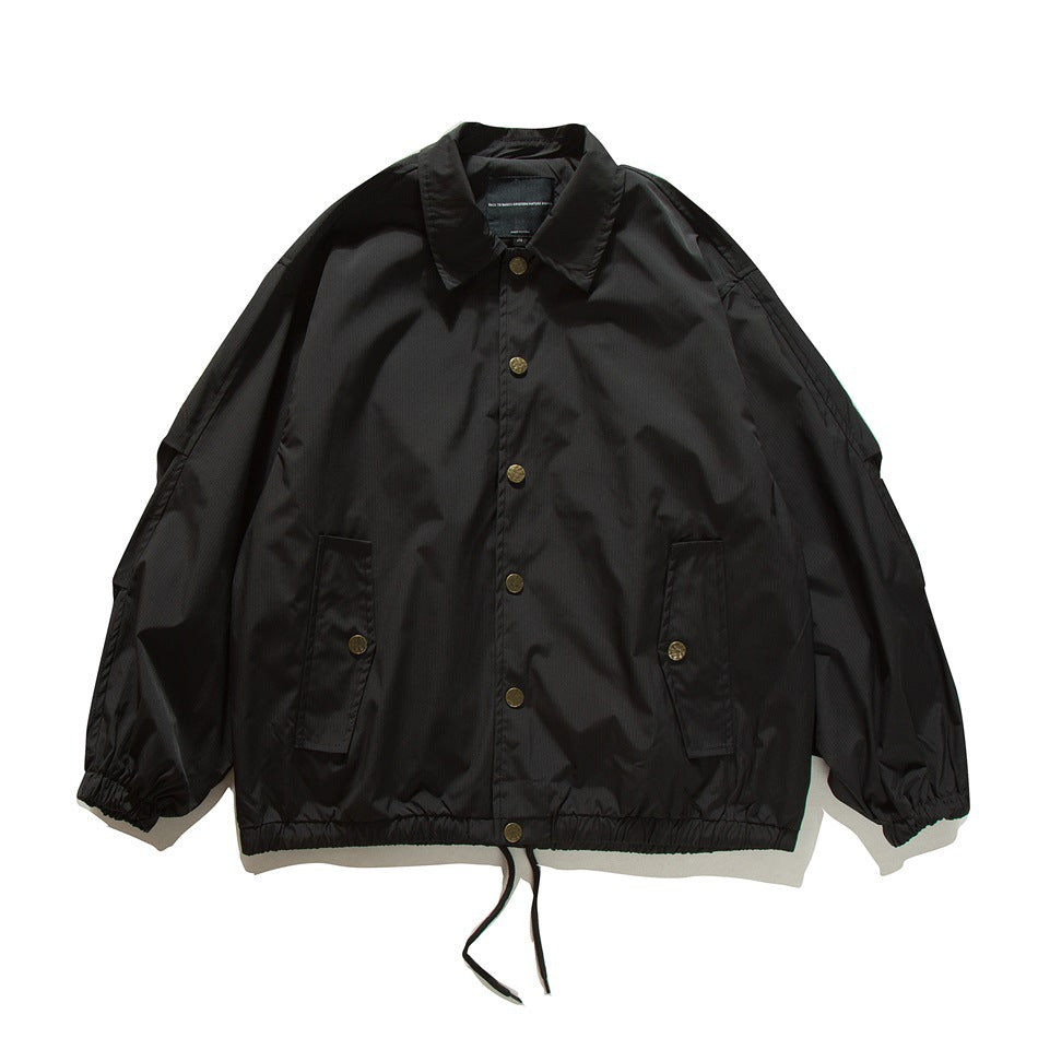 Black coach-style jacket flat lay, front view with gold buttons, flap pockets, elastic cuffs and drawstring hem