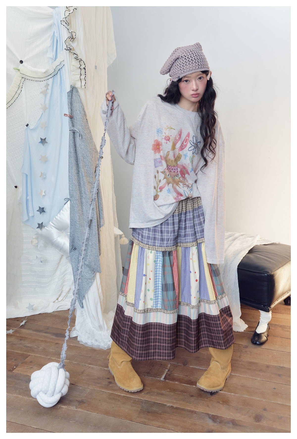 Full-length model wearing a tiered multicolor patchwork skirt and illustrated long-sleeve top with a knit cap.