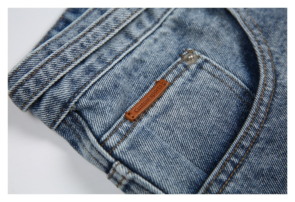 Close-up of a faded blue denim pocket with contrast stitching, a metal rivet, and a small brown label.