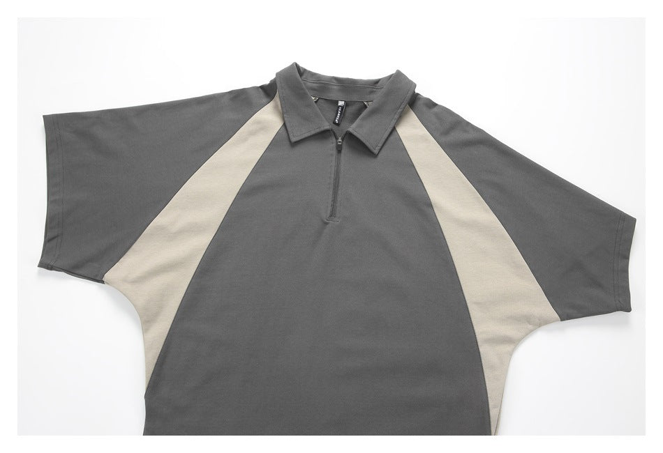 Front flat lay of a charcoal gray short-sleeve collared top with a short zipper and beige side panels.