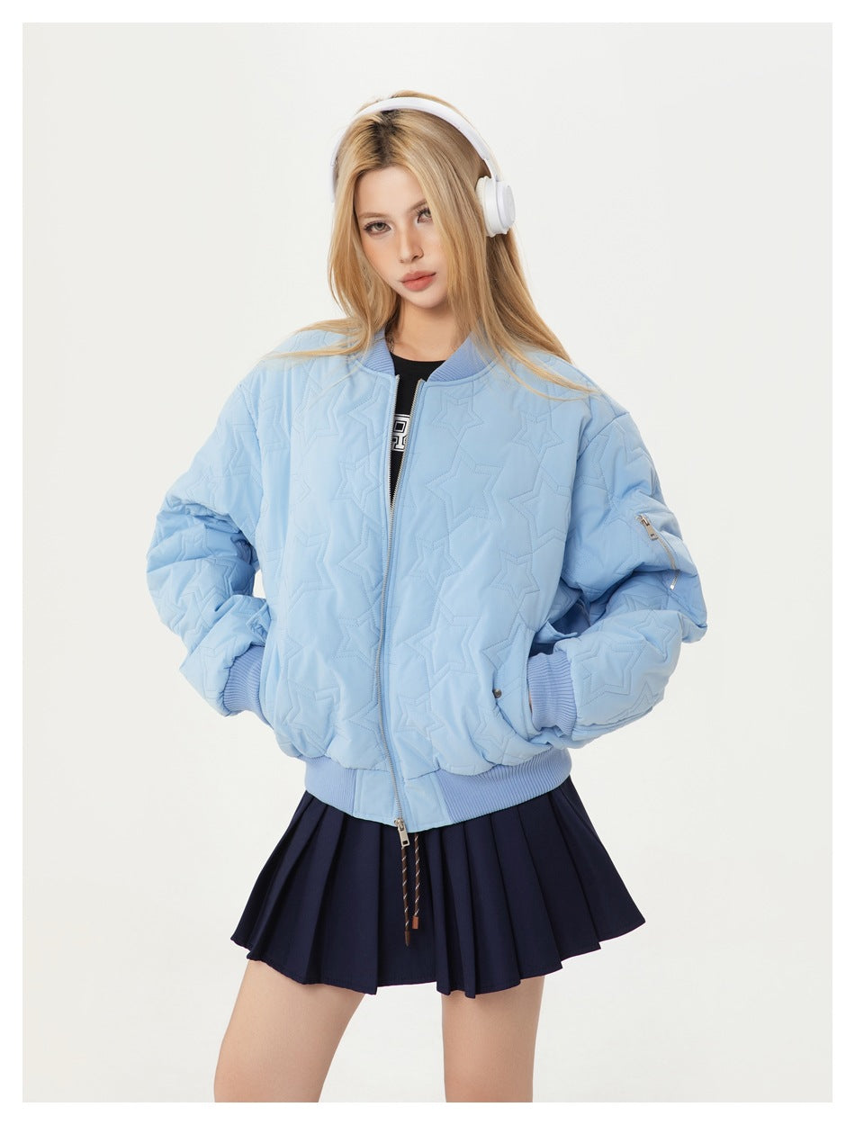 Model wearing a light blue star-quilted bomber jacket with ribbed trim, styled with a navy pleated skirt.